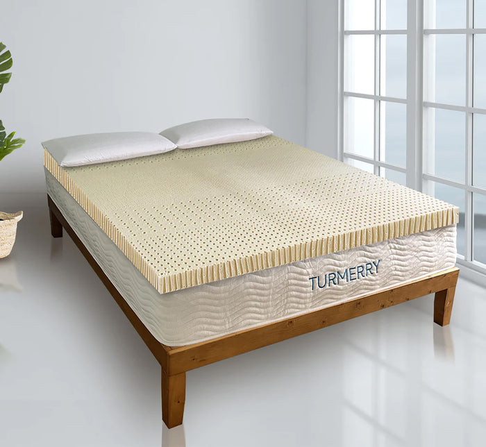 Turmerry Organic Latex Mattress Topper on wooden bed frame with perforated latex surface and white pillows in bright bedroom.