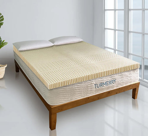 Turmerry Organic Latex Mattress Topper on wooden bed frame with perforated latex surface and white pillows in bright bedroom.
