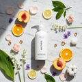 Apotheke Canvas Body Lotion 480ml flat lay — luxury hotel body lotion with lily of the valley rose violet citrus peach amber musk scent elements on white marble