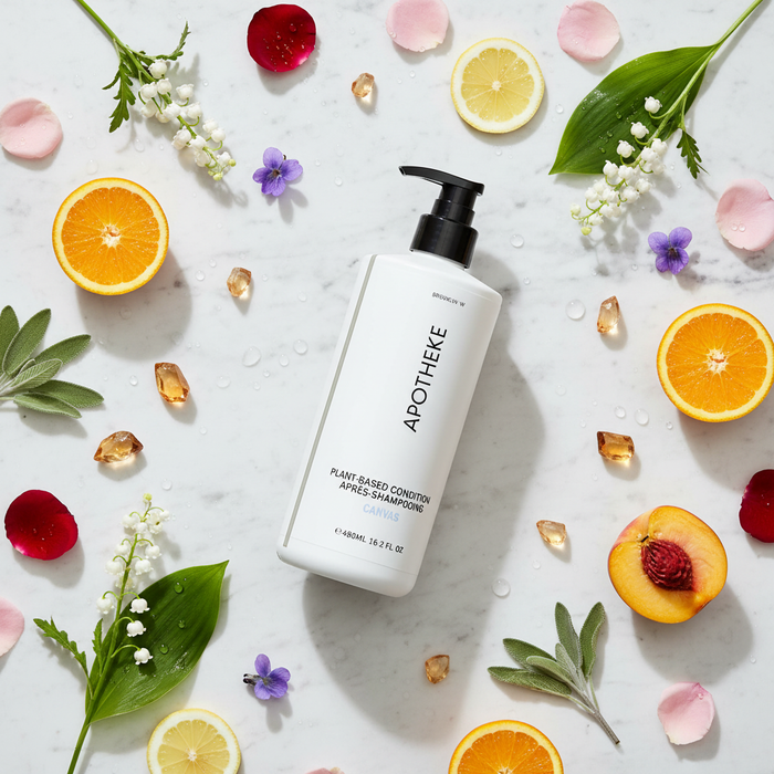 Apotheke Canvas hotel conditioner 480ml flat lay on white marble with lily of the valley rose violet citrus peach amber scent elements — luxury plant-based hair care