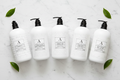 luxury hotel bath set featuring five elegant white bottles on a marble surface with green leaves.