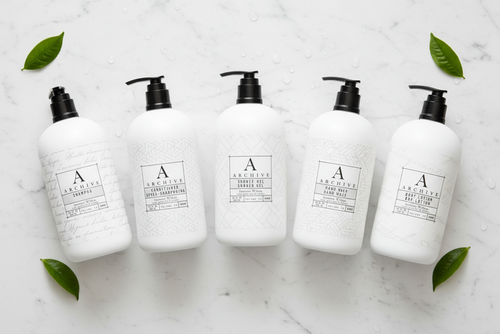 luxury hotel bath set featuring five elegant white bottles on a marble surface with green leaves.