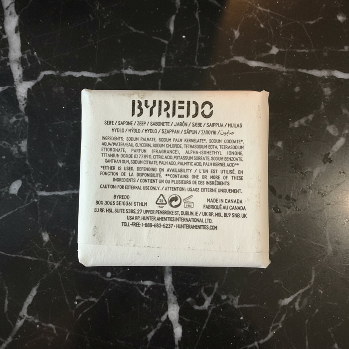 The back of a BYPEDO skincare pouch, showing the product name, ingredients list, and manufacturer details in black text on a white background, placed on a dark textured surface.