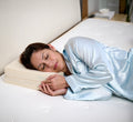 Woman sleeping on her side on Turmerry Cuboid Pillow wearing light blue silk pajamas in modern bedroom.