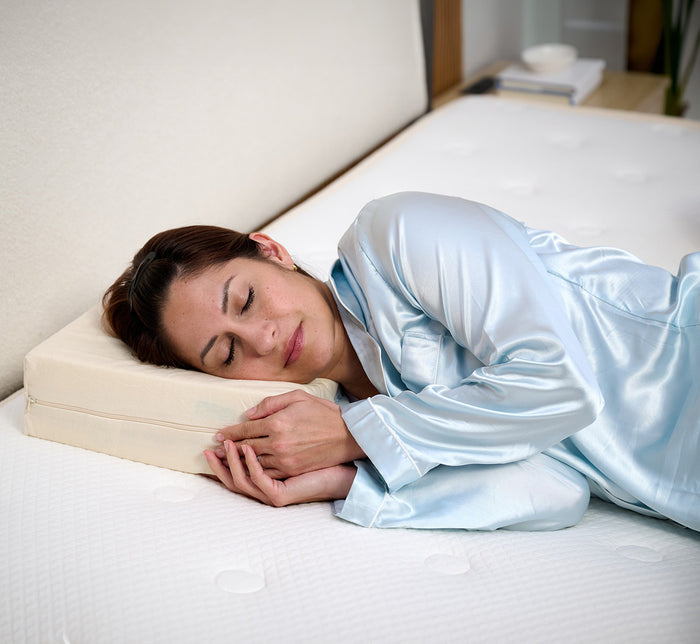 Woman sleeping on her side on Turmerry Cuboid Pillow wearing light blue silk pajamas in modern bedroom.