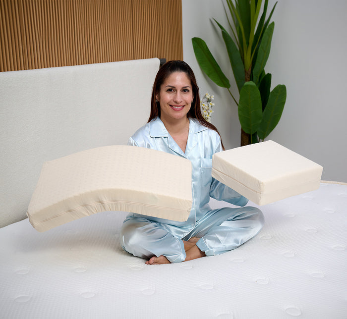 Woman holding two Turmerry Cuboid Pillows, short and long, sitting on bed in a modern bedroom.