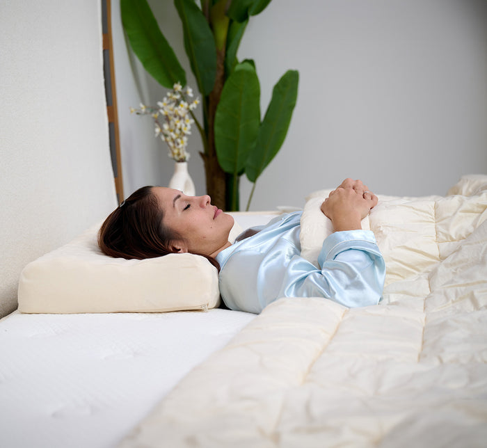 Woman resting on her back on Turmerry eggcrate latex contour pillow with green plant in background.