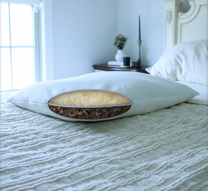 Turmerry Hybrid Pillow cross section on a bed in modern bedroom, showing cream wool and dark buckwheat layers inside.