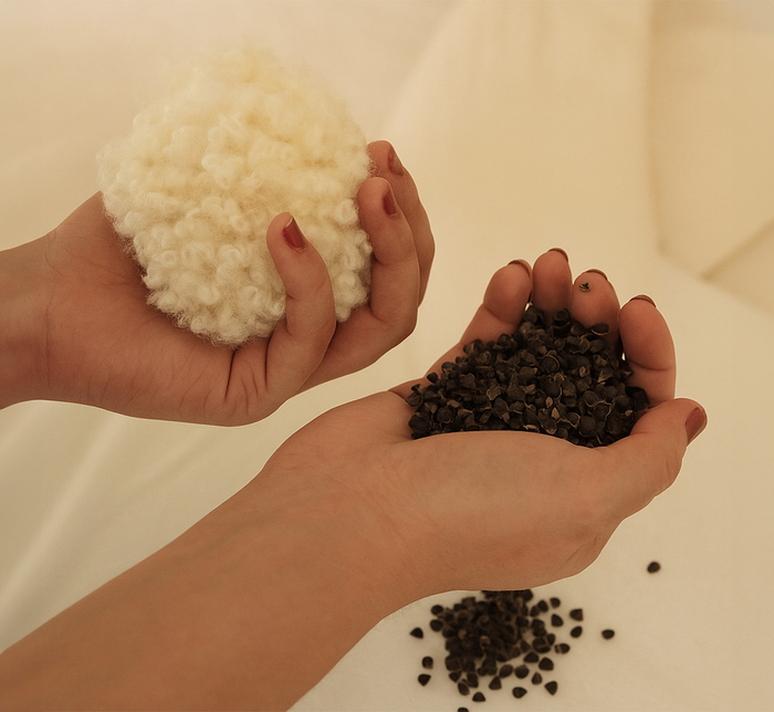 Two hands, with wool fill in one hand and buckwheat hull fill on the other, atop a white bed.