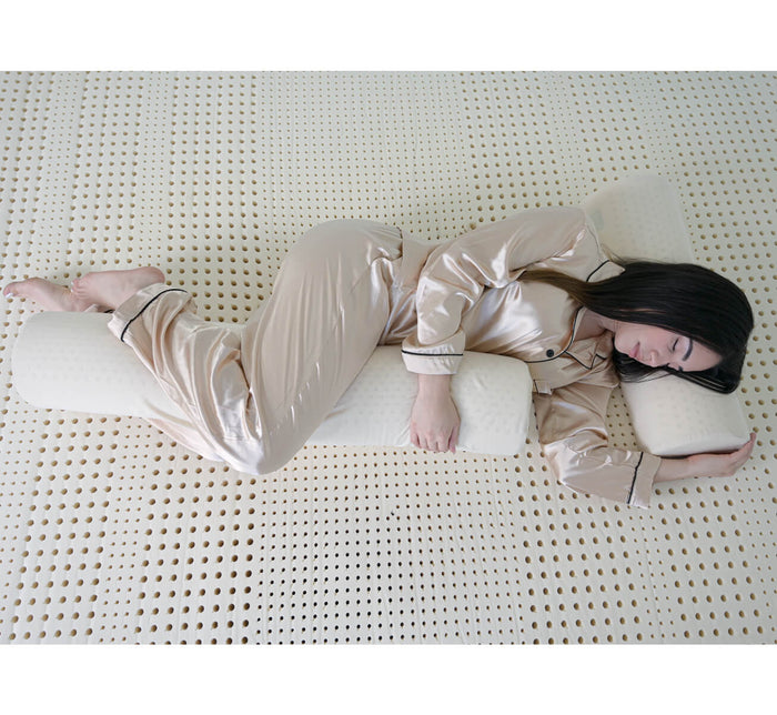 Woman sleeping on her side using Turmerry latex body pillow for leg and knee support on mattress.