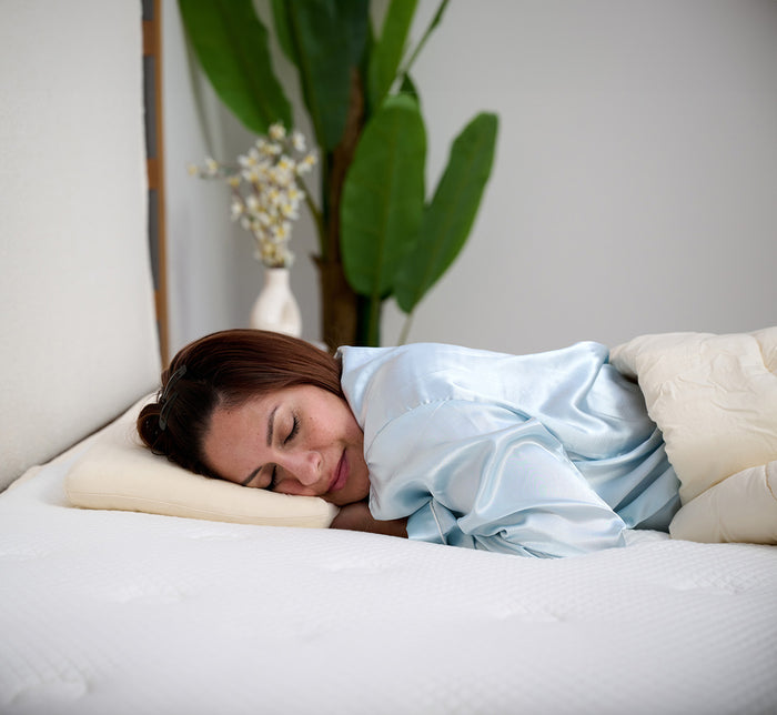 Woman resting on stomach on Turmerry low profile toddler pillow in modern bedroom setting.