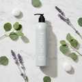 Marriott 39 North Hand & Body Wash 12 oz bottle surrounded by green leaves and purple flowers on marble surface.