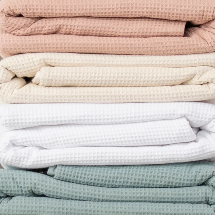 4 different colors of Naturepedic Organic Cotton Waffle Blankets stacked on top of eachother