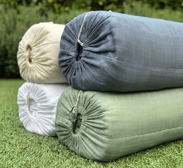 Turmerry organic cotton crinkled reversible muslin blankets in ivory, white, blue, and green rolled on grass.