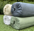 Turmerry organic cotton crinkled reversible muslin blankets in ivory, white, blue, and green rolled on grass.