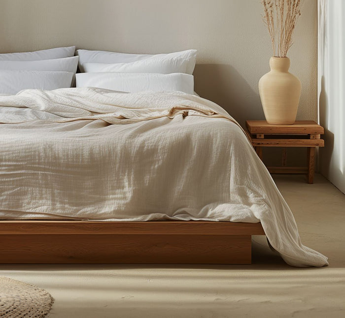 Ivory Turmerry organic cotton crinkled reversible muslin blanket on bed with white pillows and wood nightstand.