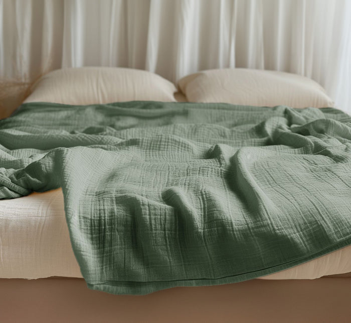 Green Turmerry organic cotton crinkled reversible muslin blanket on bed with cream pillows and white curtains.