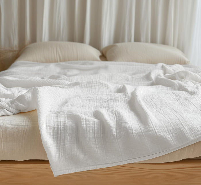 White Turmerry organic cotton crinkled reversible muslin blanket on bed with cream pillows and white curtains.