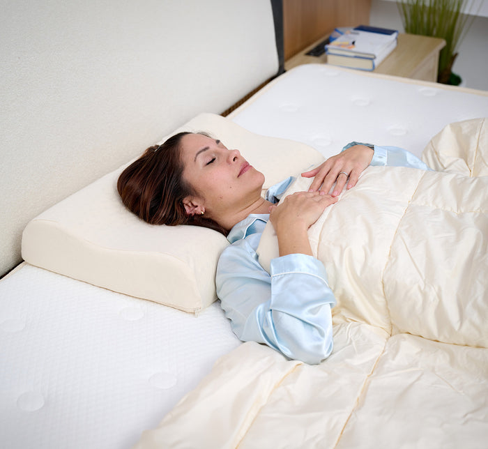 Woman lying on her back on Turmerry Latex Contour Pillow with cream cover, in modern bedroom.