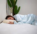 Woman sleeping on her side on Turmerry latex donut pillow with green plant in background.