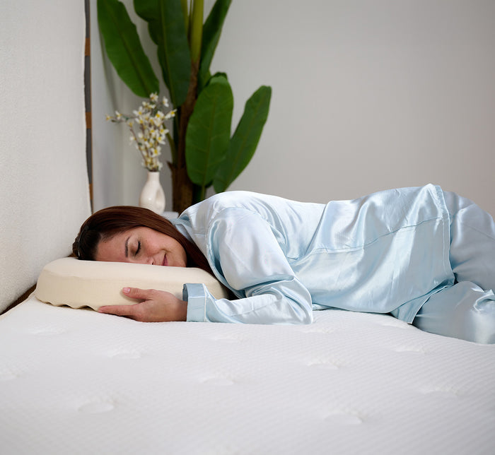 Woman sleeping on her side on Turmerry latex donut pillow with green plant in background.