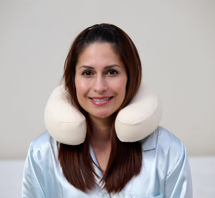 Woman wearing Turmerry latex travel neck pillow with white cover around neck against gray background.