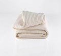 Cream-colored Turmerry Organic Striped Chenille Herringbone Blanket Throw folded and placed on a light gray background.
