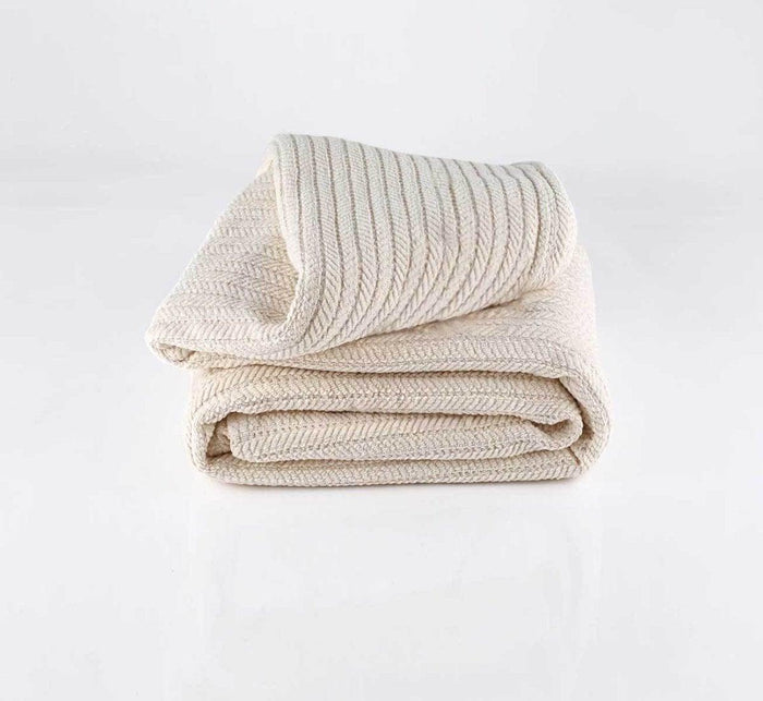Cream-colored Turmerry Organic Striped Chenille Herringbone Blanket Throw folded and placed on a light gray background.
