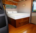 Turmerry Latex RV Mattress Topper on wood bed frame in motorhome bedroom with window views and cream interior walls.