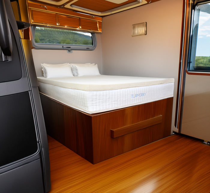 Turmerry Latex RV Mattress Topper on wood bed frame in motorhome bedroom with window views and cream interior walls.