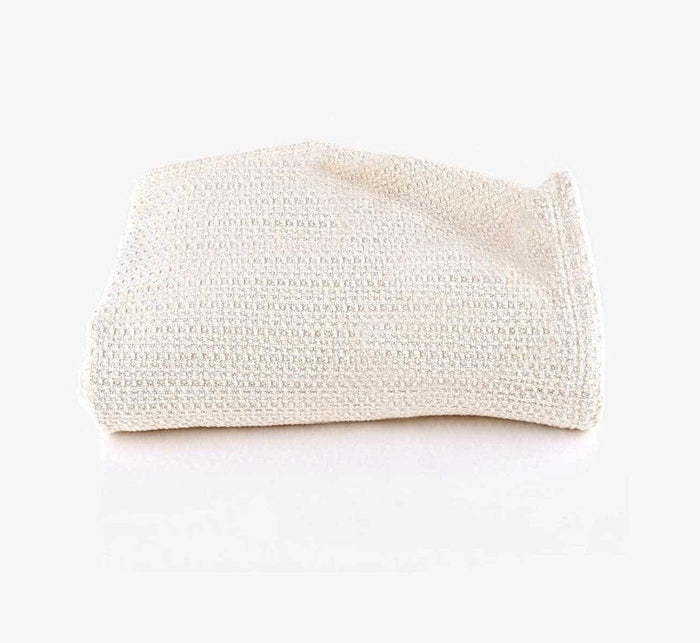 Cream-colored Turmerry Waffle Weave Organic Cotton Blanket Throw folded and placed on a light gray background.