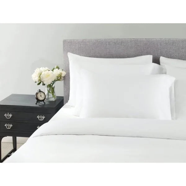 Wynrest Microfiber Pillowcase in white, standard size 42x36", placed on a bed with black nightstand and flowers.