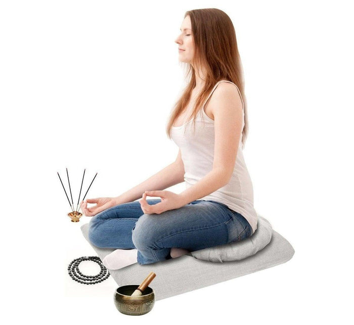 Woman sitting in lotus position on Turmerry zafu and zabuton pillow, meditating, with yoga accessories beside.